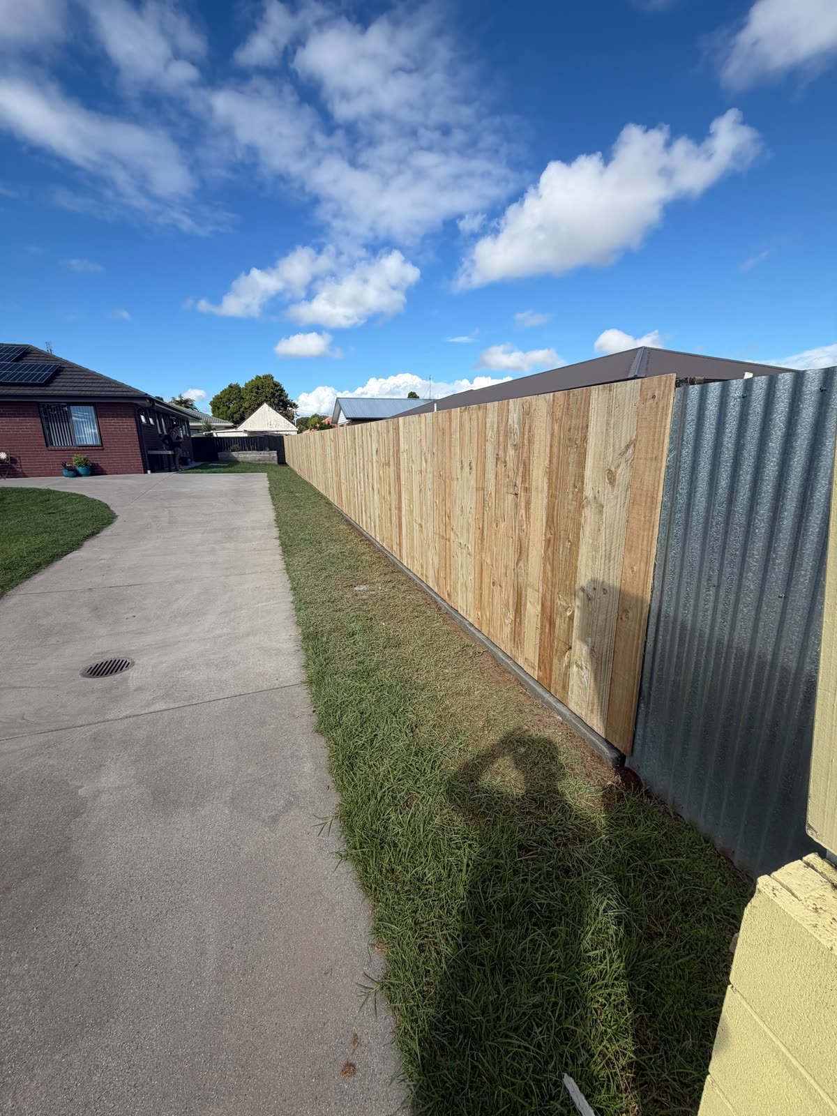 New timber paling fence in Papakura running along a driveway, tied into an existing corrugated iron fence
