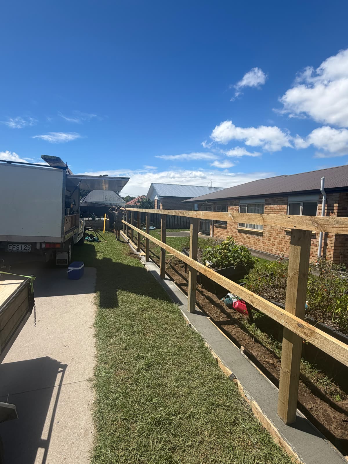 Boundary fence framed up between a driveway and a neighbour's garden in Papakura, posts and rails in, palings still to go